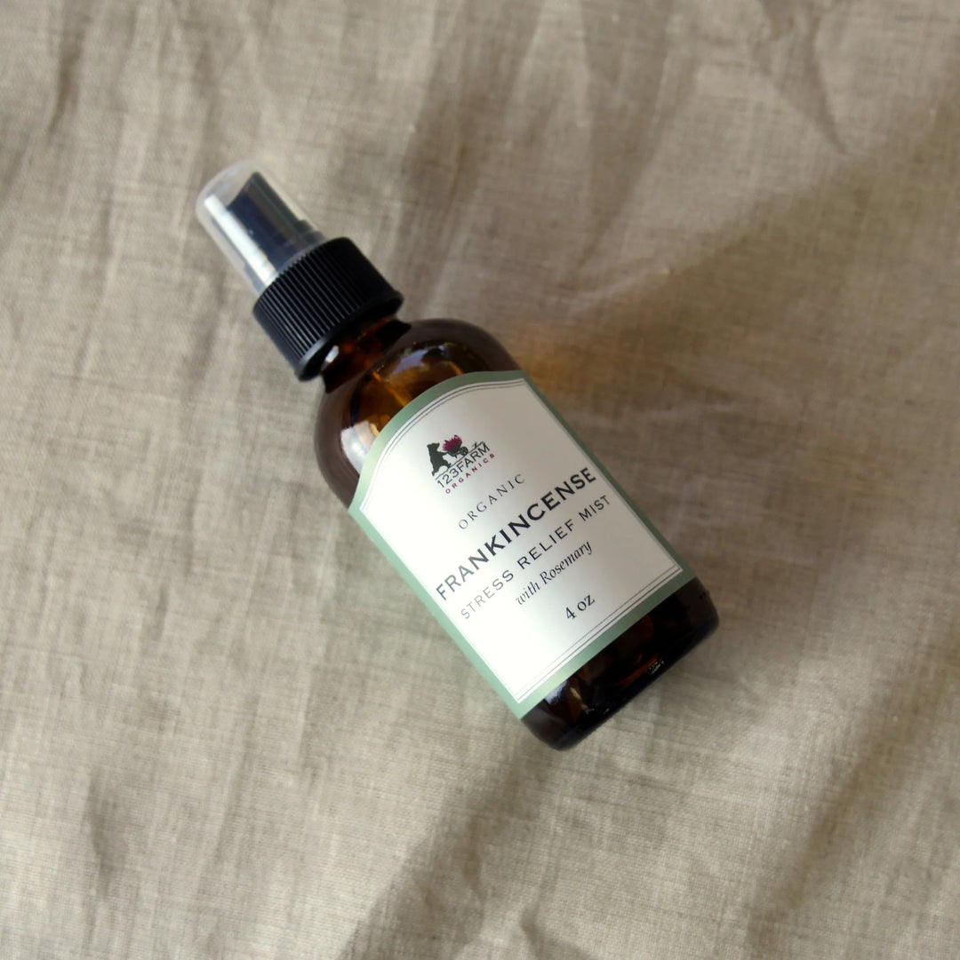 An amber spray bottle of 123 Farm Organic Stress Relief Mist with Rosemary is on a beige linen background. Available at Luca Essentials in Los Angeles.
