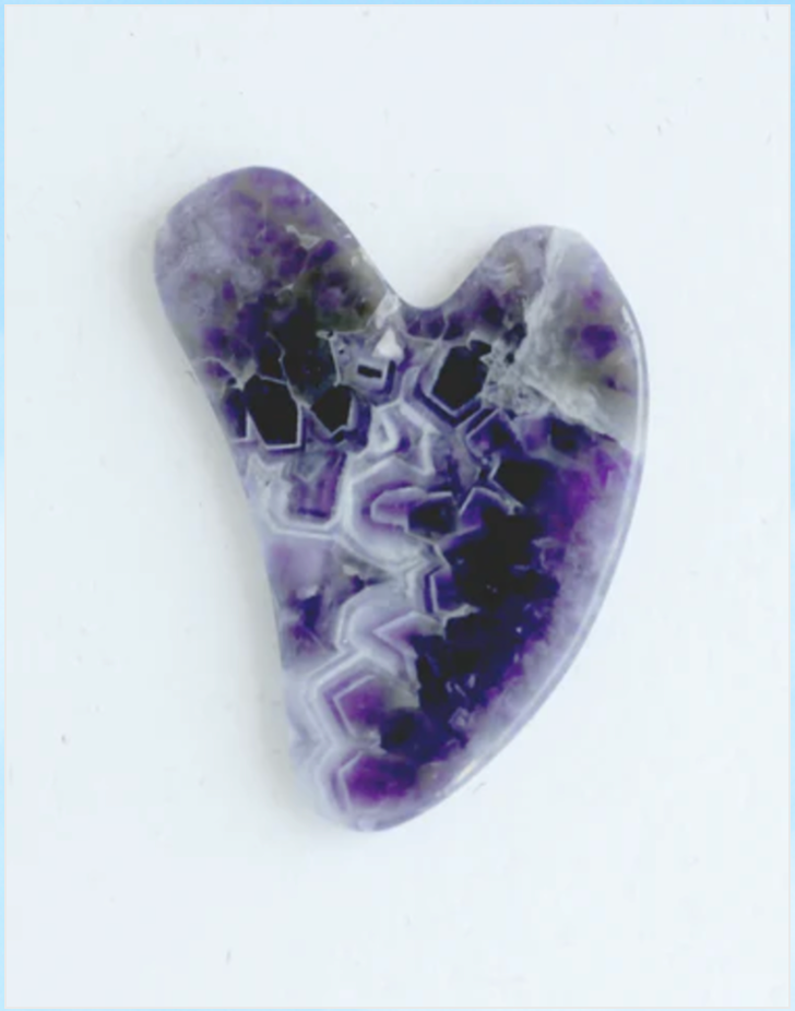 An Amethyst Gua Sha on a white background. Bamboo Switch is available at Luca Essentilas in Los Angeles.