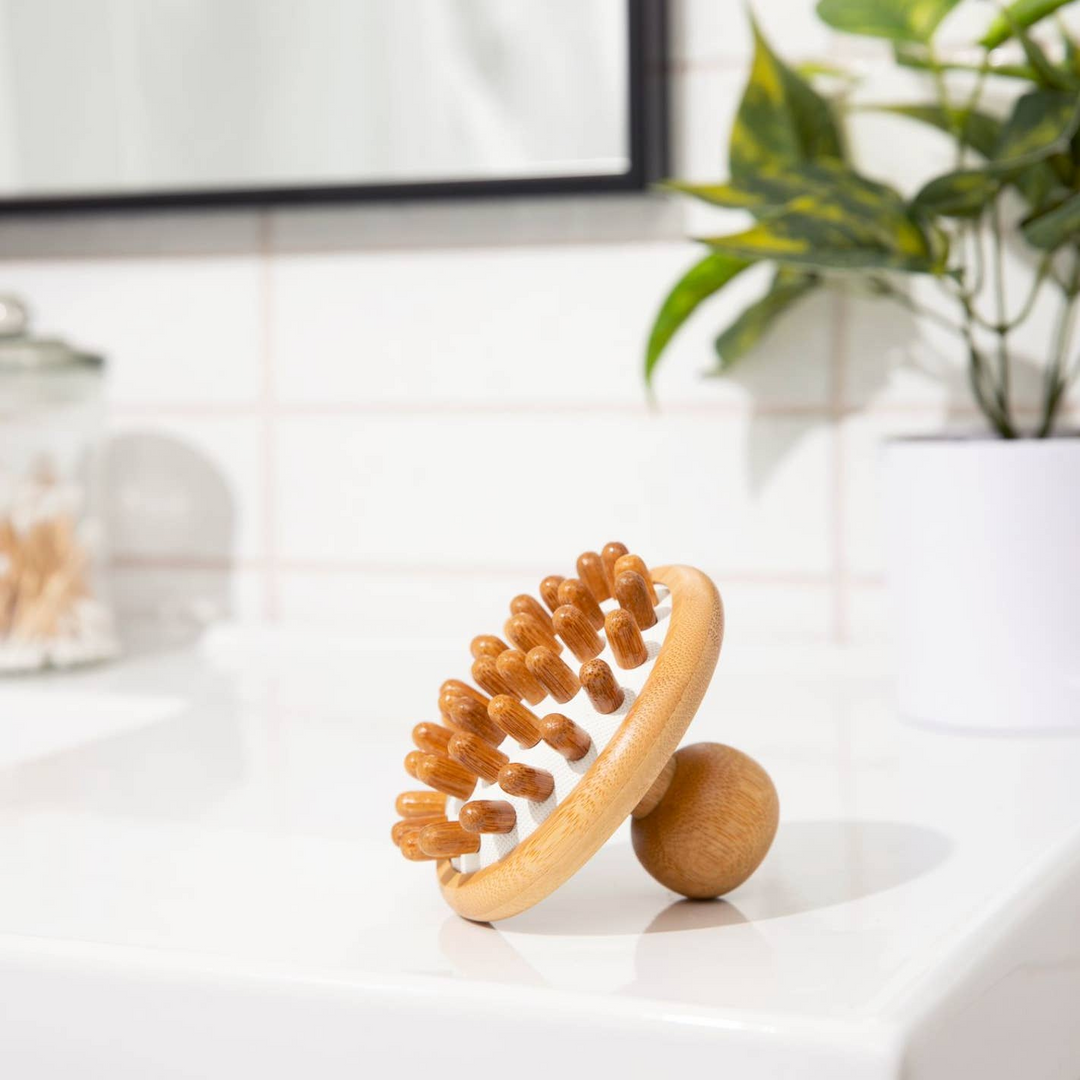 A bamboo stimulating scalp massager with rounded bristles, placed on a white surface, likely a bathroom counter.  Bamboo Switch is available at Luca Essentials in Los Angeles.