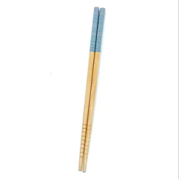 A pair of bamboo chopsticks with a beige and blue patterned grip. Bamboo Switch is available at Luca Essentials in Los Angeles.