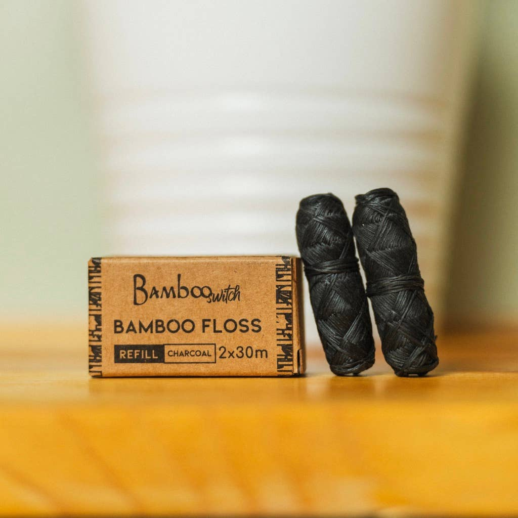 Two rolls of charcoal dental floss refills next to their packaging box, which reads 'Bamboo Floss' and has a 'Charcoal' label. Bamboo Switch is available at Luca Essentials in Los Angeles.