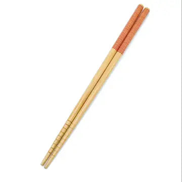 A pair of bamboo chopsticks with a beige and red patterned grip. Bamboo Switch is available at Luca Essentials in Los Angeles.