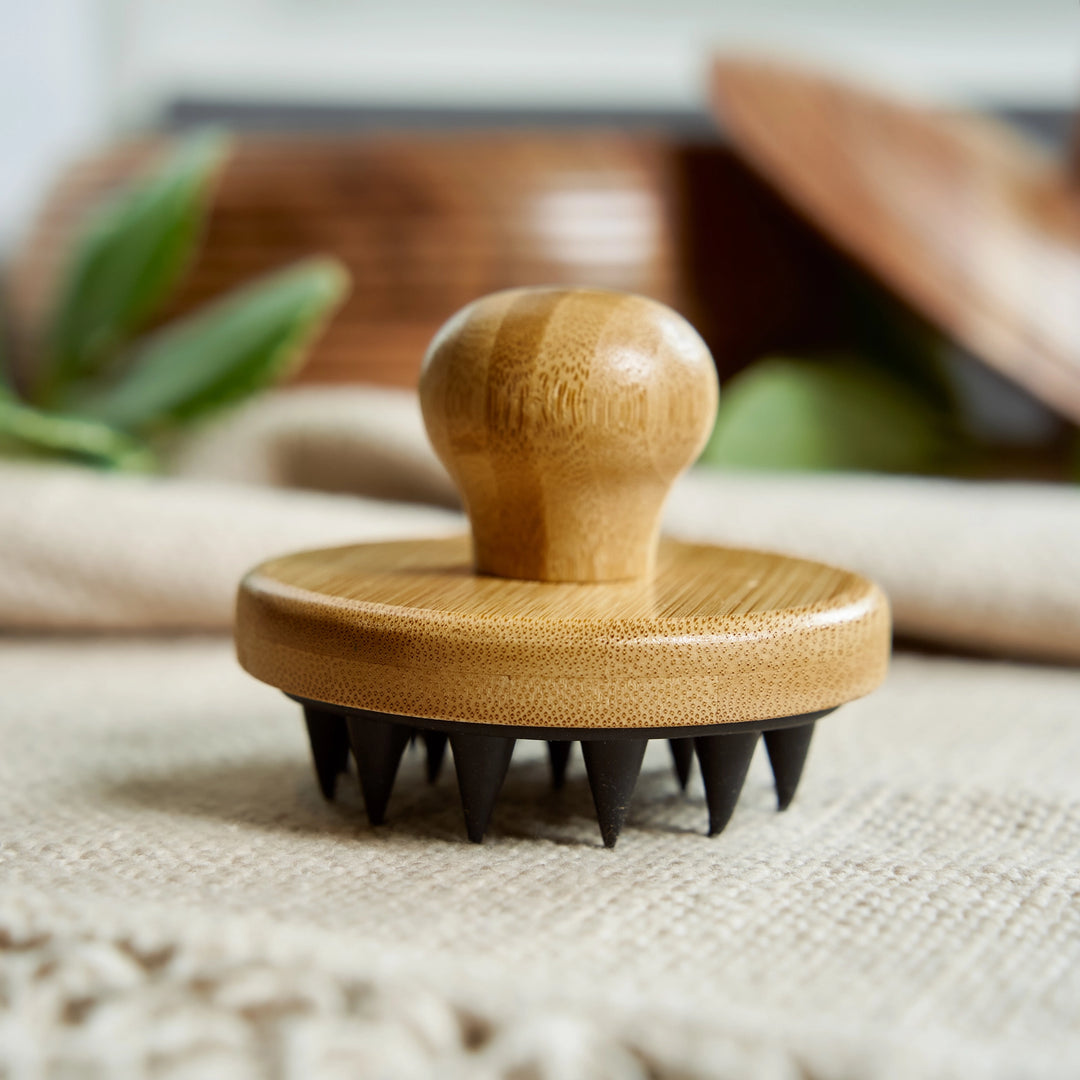 Wooden massage tool with black bristles on a textured surface. Bamboo Switch is available at Luca Essentials in Los Angeles.