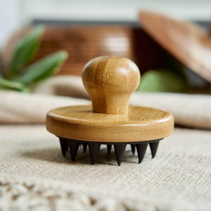 Wooden massage tool with black bristles on a textured surface. Bamboo Switch is available at Luca Essentials in Los Angeles.