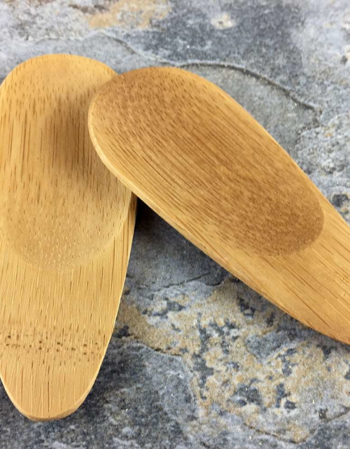 Two oval-shaped bamboo spatulas lying on a textured surface. Bamboo Switch is available at Luca Essentials in Los Angeles.