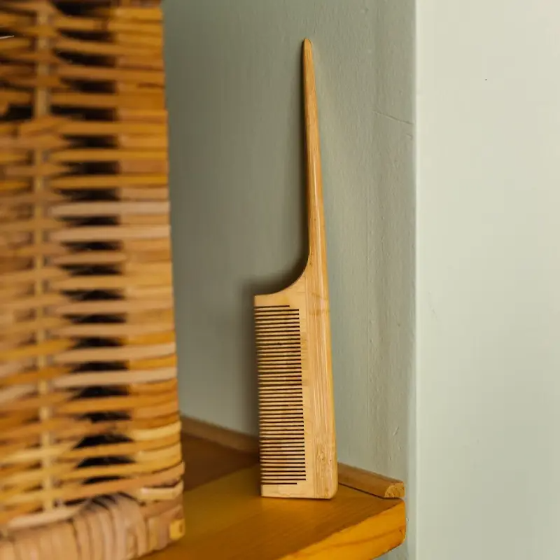 A bamboo styling comb placed upright on a shelf, with a woven basket in the background. Bamboo Switch is available at Luca Essentials in Los Angeles.