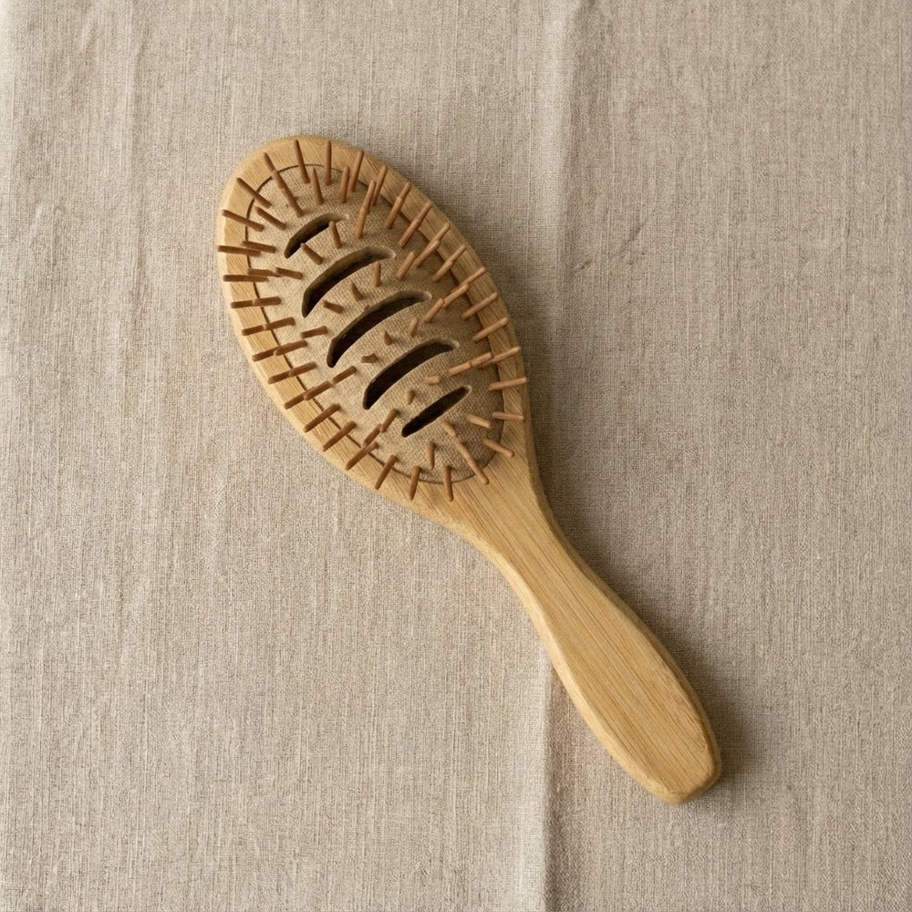 Wooden hairbrush on a beige fabric background. Bamboo Switch is available at Luca Essentials in Los Angeles.