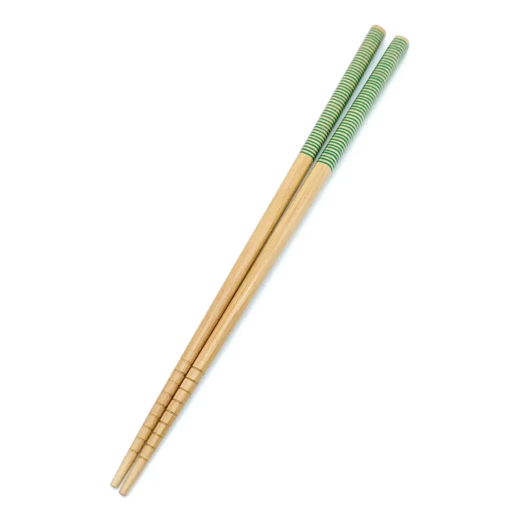 A pair of bamboo chopsticks with a beige and green patterned grip. Bamboo Switch is available at Luca Essentials in Los Angeles.