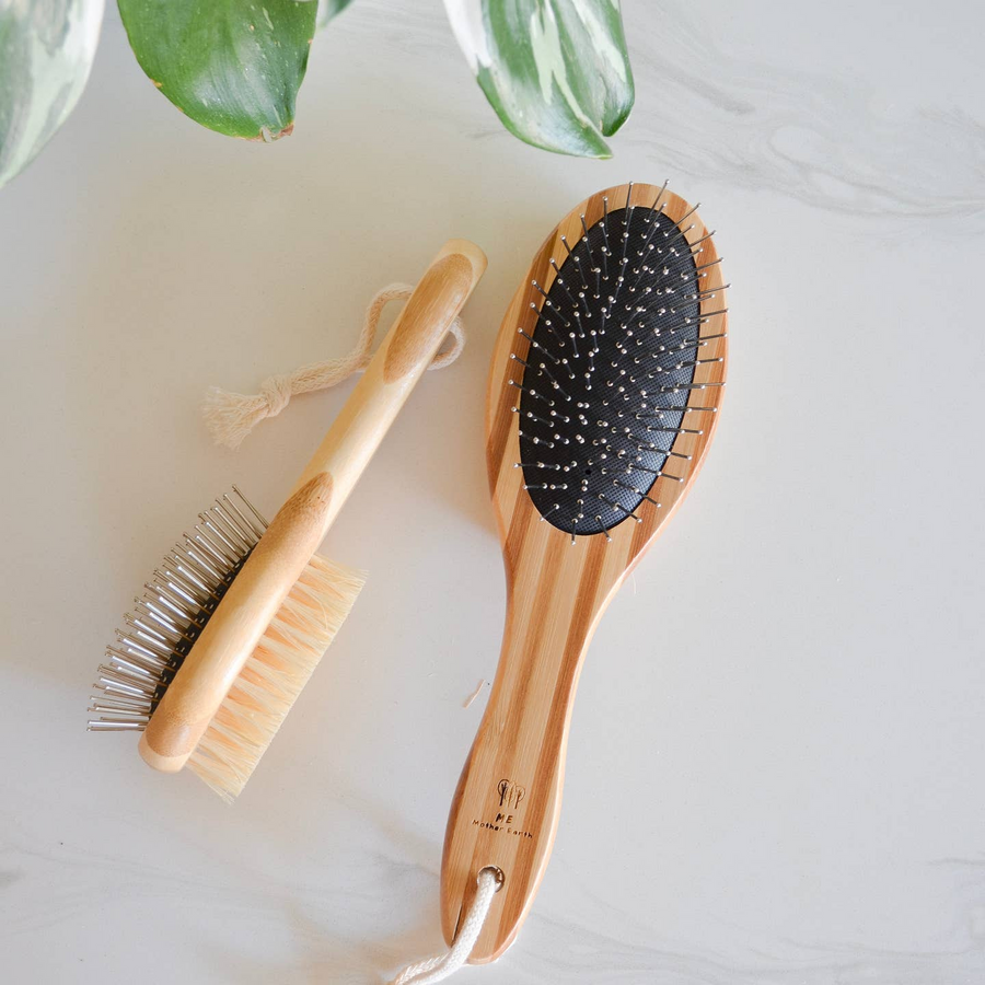 Two wooden hairbrushes on a light surface with green leaves in the background. Bamboo Switch is available at Luca Essentials in Los Angeles.
