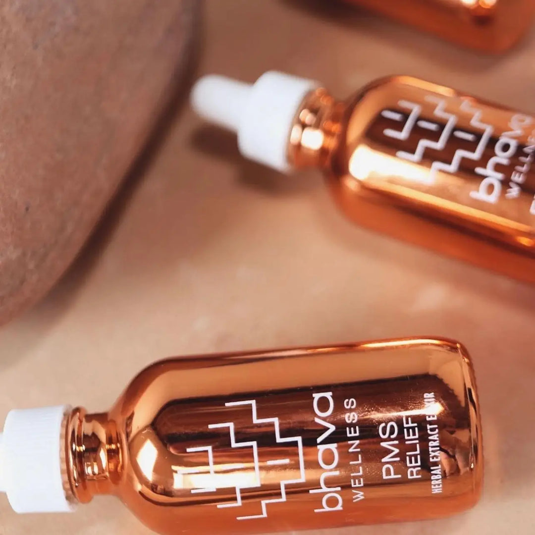 Two rose gold bottles of Bhava Wellness PMS Relief Herbal Elixirs lie on pink surface. Bhava Wellness is available at Luca Essentials in Los Angeles.