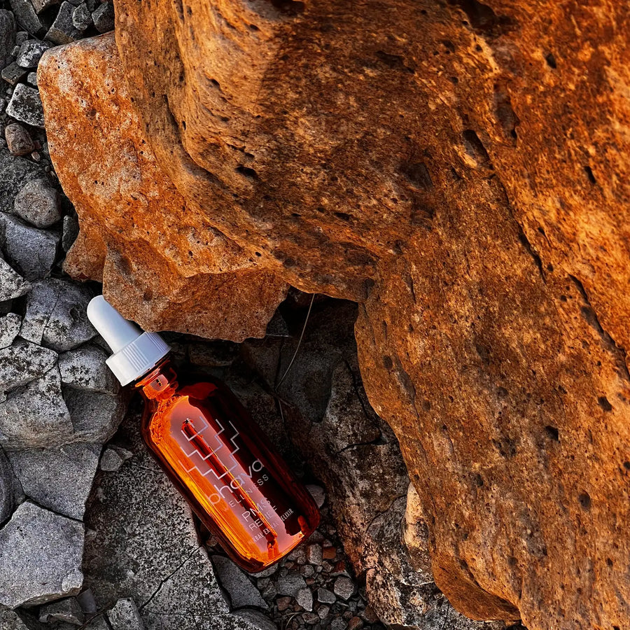 A rose gold bottle of Bhava Wellness PMS Relief Herbal Elixir with a dropper, placed on a rocky suxrface. Bhava Wellness is available at Luca Essentials in Los Angeles.