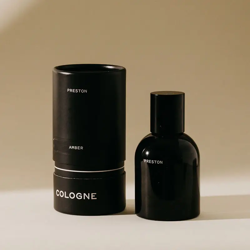 Black cologne bottle and cylindrical container on a beige background. Available at Luca Essentials in Los Angeles. 