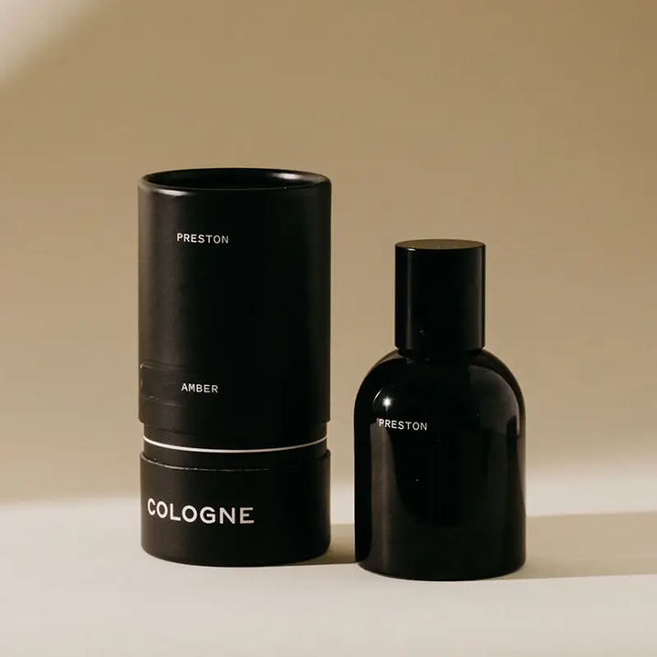 Black cologne bottle and cylindrical container on a beige background. Available at Luca Essentials in Los Angeles. 