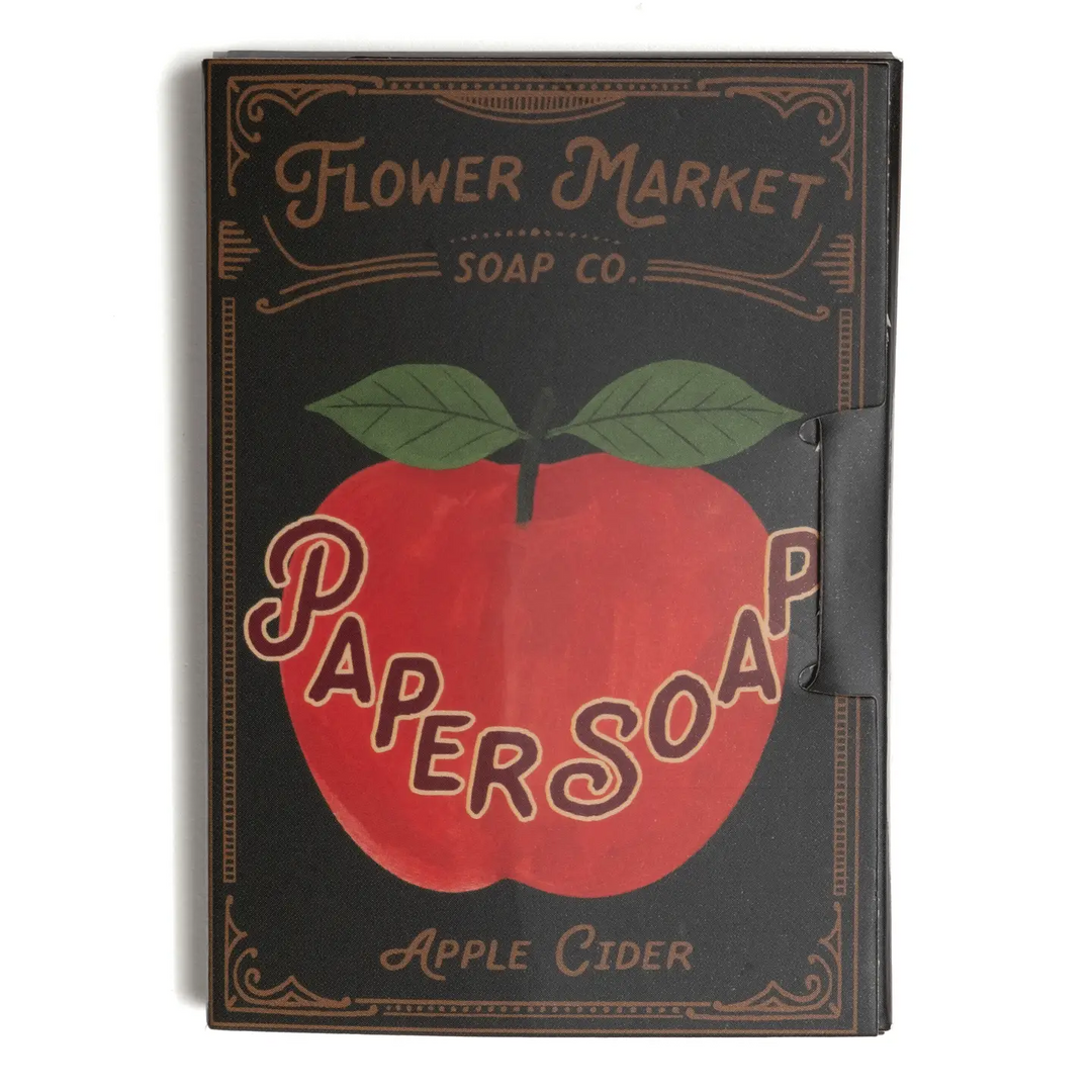 A rectangular soap bar in a vintage-style black box labeled 'Flower Market Soap Co.' with a large red apple graphic and the words 'Paper Soap' and 'Apple Cider.' Available at Luca Essentials in Los Angeles.