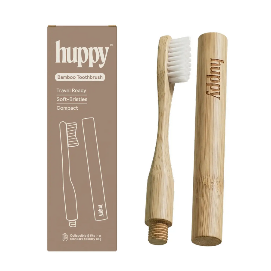 A bamboo toothbrush set with a natural wood handle, white bristles, a threaded end, and a matching bamboo travel case. The set is displayed next to its brown cardboard packaging box on a plain white background. Available at Luca Essentials in Los Angeles. 