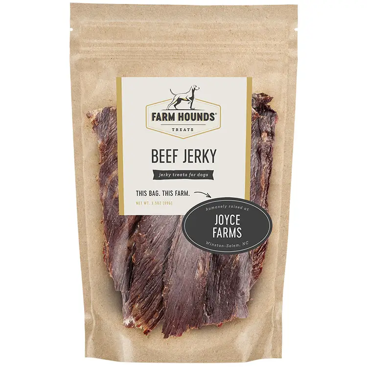 A bag of Farm Hounds Beef Jerky treats for dogs, in a brown kraft stand-up pouch with a clear window showing the jerky slices inside. The front label includes the Farm Hounds logo and a black oval badge that says 'Humanely raised by Joyce Farms'. Available at Luca Essentials in Los Angeles. 