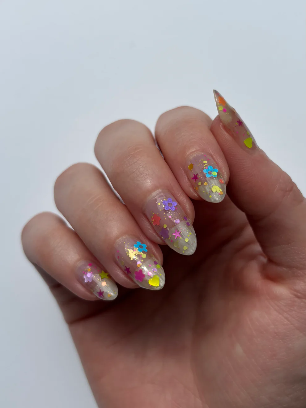 Hand with colorful glittery nail polish on a white background. Available at Luca Essentials in Los Angeles. 