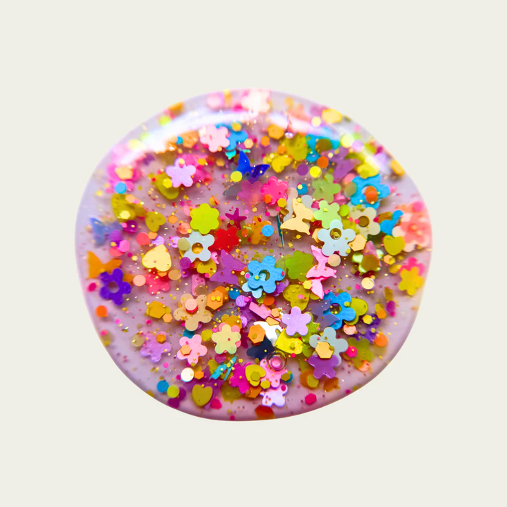 Round swatch with colorful floral and star-shaped confetti on a light gray background. Available at Luca Essentials in Los Angeles. 