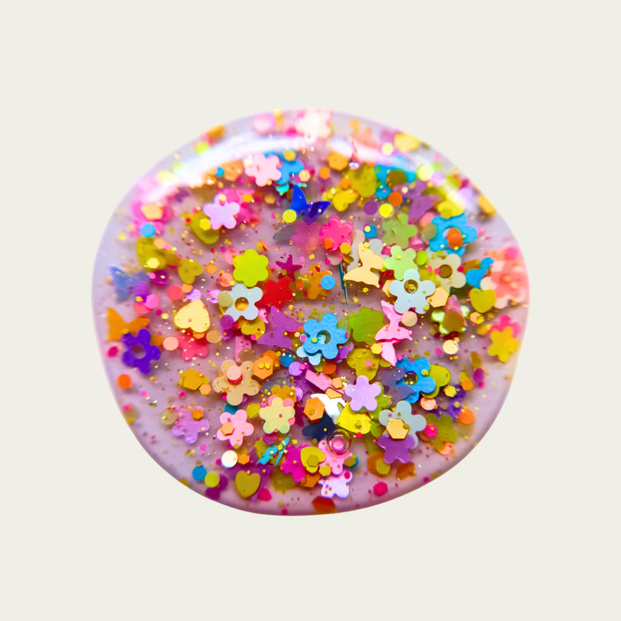 Round swatch with colorful floral and star-shaped confetti on a light gray background. Available at Luca Essentials in Los Angeles. 