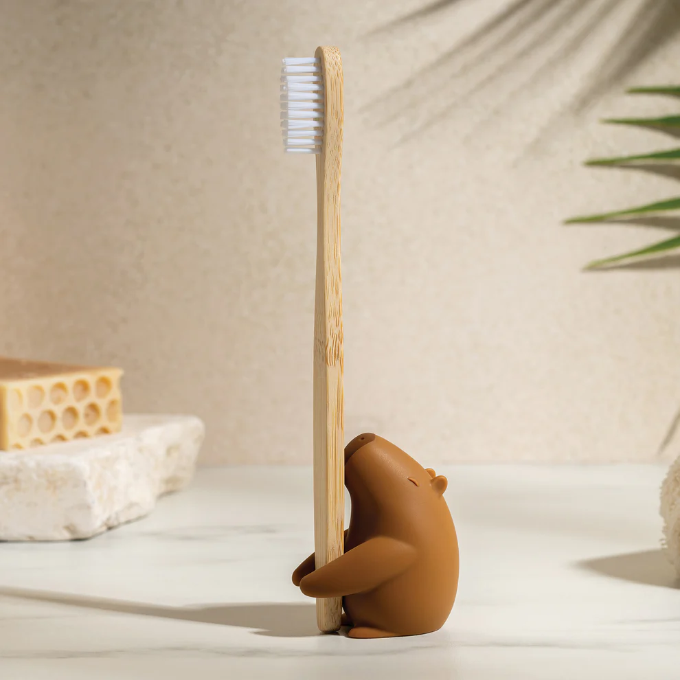 Bamboo toothbrush with a cabybara-shaped holder on a neutral background. Available at Luca Essentials in Los Angeles. 