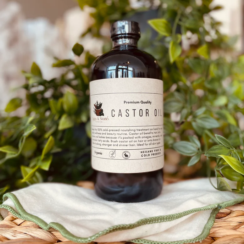 Bottle of castor oil on a woven surface with greenery in the background. Available at Luca Essentials in Los Angeles. 