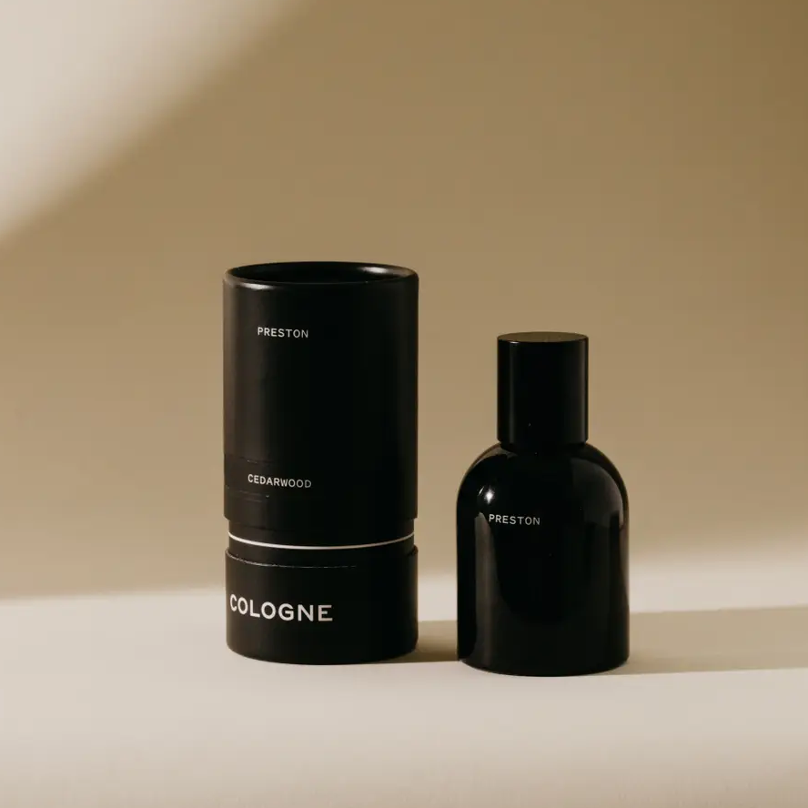 Black perfume bottle and cylindrical container on a beige background. Available at Luca Essentials in Los Angeles. 