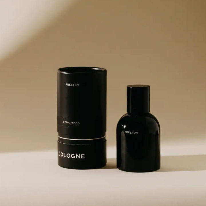 Black perfume bottle and cylindrical container on a beige background. Available at Luca Essentials in Los Angeles. 