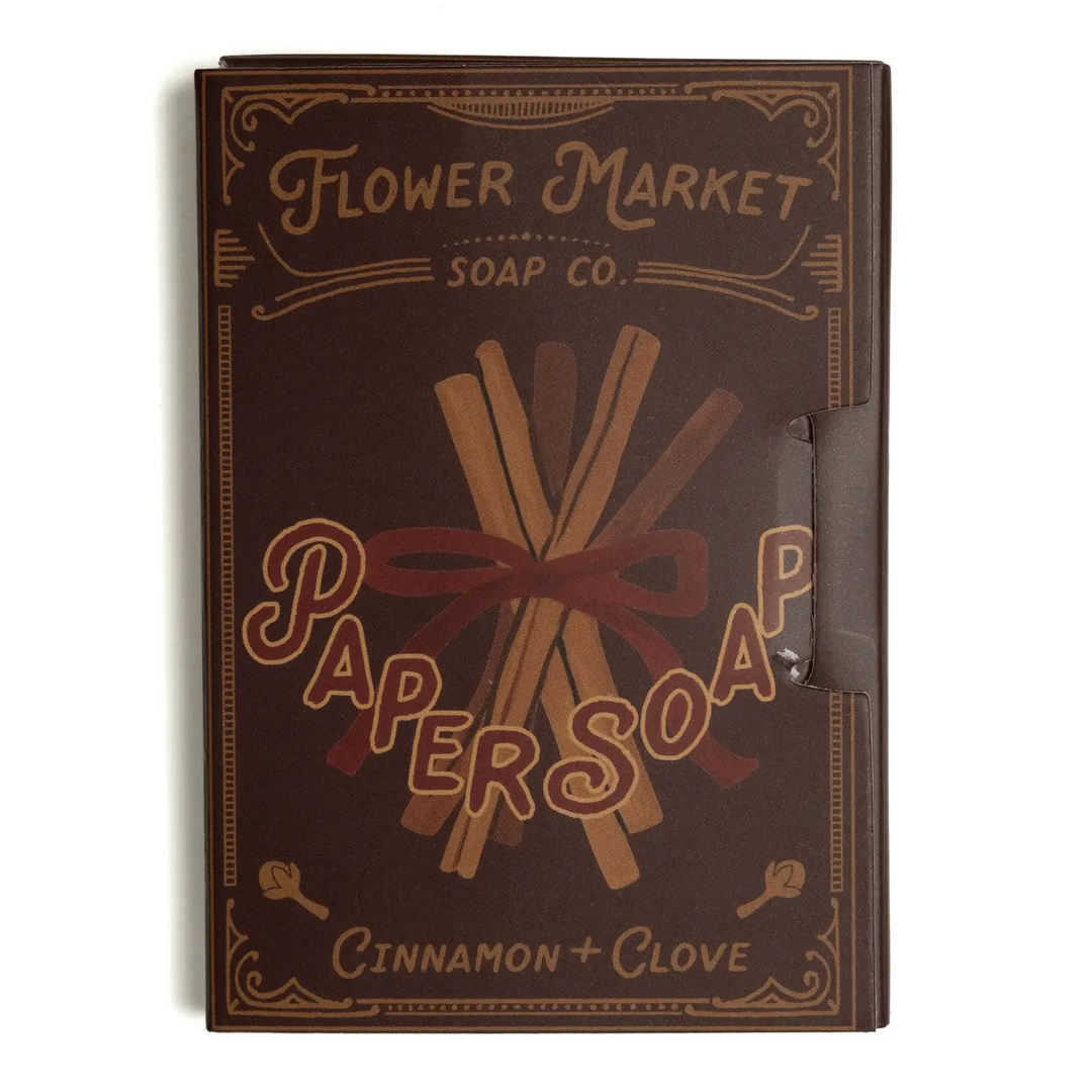 A square brown soap box for 'Flower Market Soap Co.' with a vintage-style label reading 'Paper Soap' and 'Cinnamon + Clove' on a white background. Available at Luca Essentials in Los Angeles. 