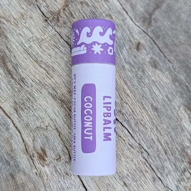 Lip balm with purple label on a wooden surface. Available at Luca Essentials in Los Angeles. 