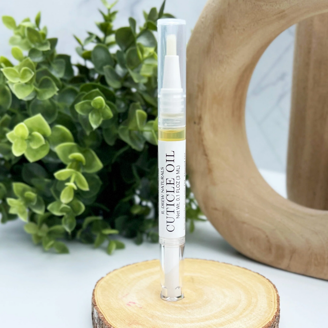 Cuticle oil bottle with brush on a wooden block with greenery in the background. Available at Luca Essentials in Los Angeles. 