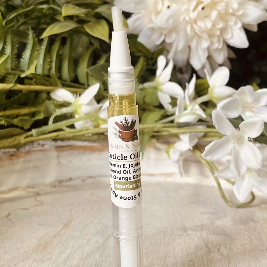 Small pen of oil with a brush on a wooden surface with white flowers in the background. Available at Luca Essentials in Los Angeles. 