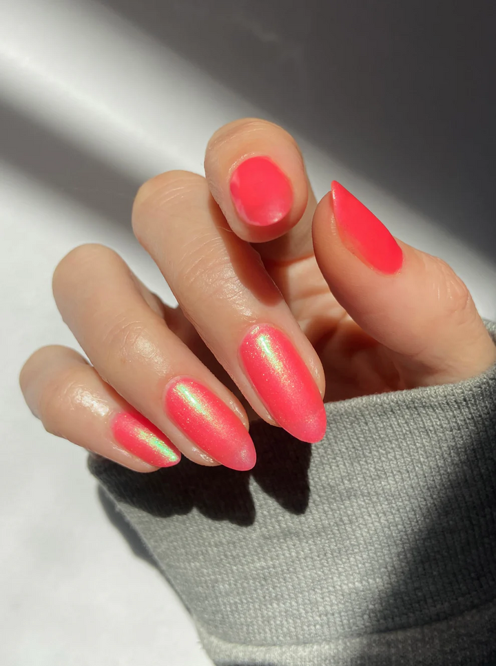 Hand with bright pink nail polish on a neutral background

This polish is a vibrant, hot pink jelly layered with fine golden microshimmer and a glowy green-to-light blueish/purple aurora shimmer. 

Available at Luca Essentials in Los Angeles.