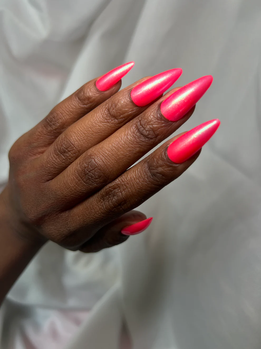 Hand with bright pink nail polish on a neutral background

This polish is a vibrant, hot pink jelly layered with fine golden microshimmer and a glowy green-to-light blueish/purple aurora shimmer. 

Available at Luca Essentials in Los Angeles.