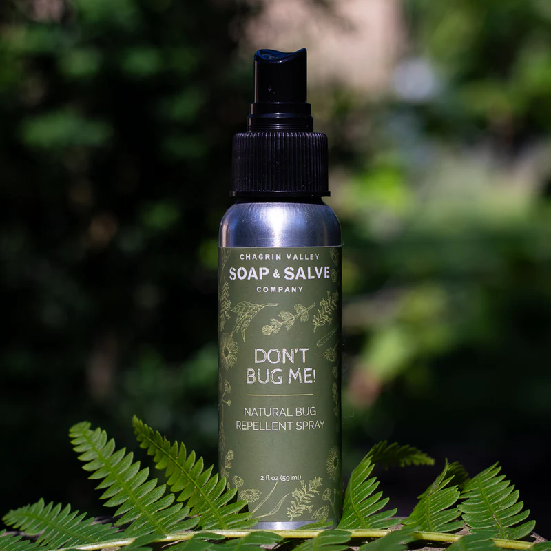 An aluminum bottle with a green label reading 'don't bug me' on a leaf with a tree in the background. Available at Luca Essentials in Los Angeles. 