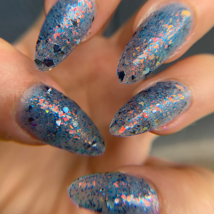 Nails with blue glittery nail polish on a neutral background. Available at Luca Essentials in Los Angeles. 