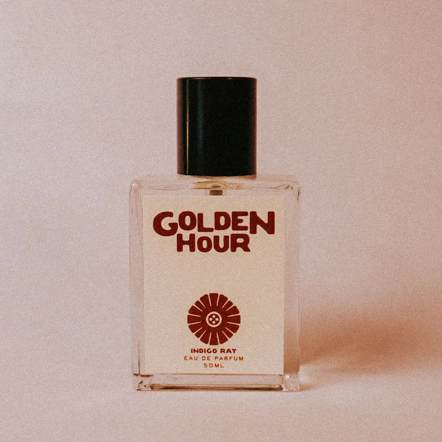 Glass perfume bottle labeled 'Golden Hour' with a black cap and red illustration on the label on a beige background. Available at Luca Essentials in Los Angeles. 