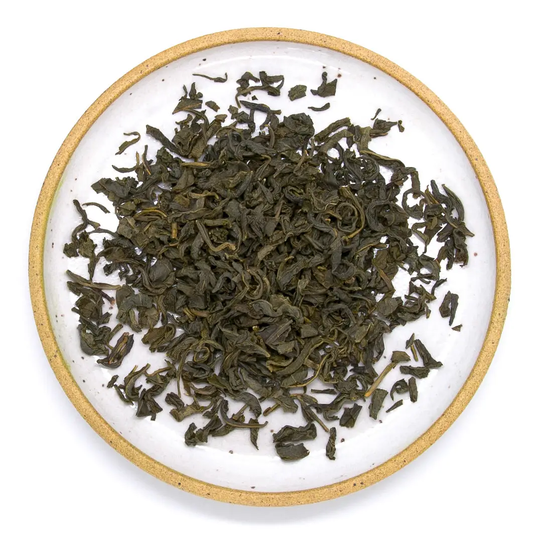 Dry green tea leaves on a white plate with a tan rim. Available at Luca Essentials in Los Angeles. 