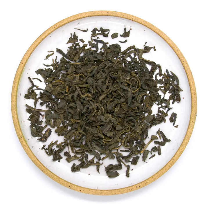 Dry green tea leaves on a white plate with a tan rim. Available at Luca Essentials in Los Angeles. 