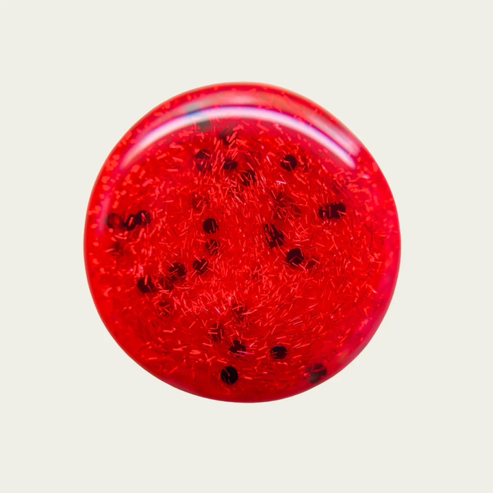 Red nail polish swatch with black specks on a light gray background. Available at Luca Essentials in Los Angeles. 