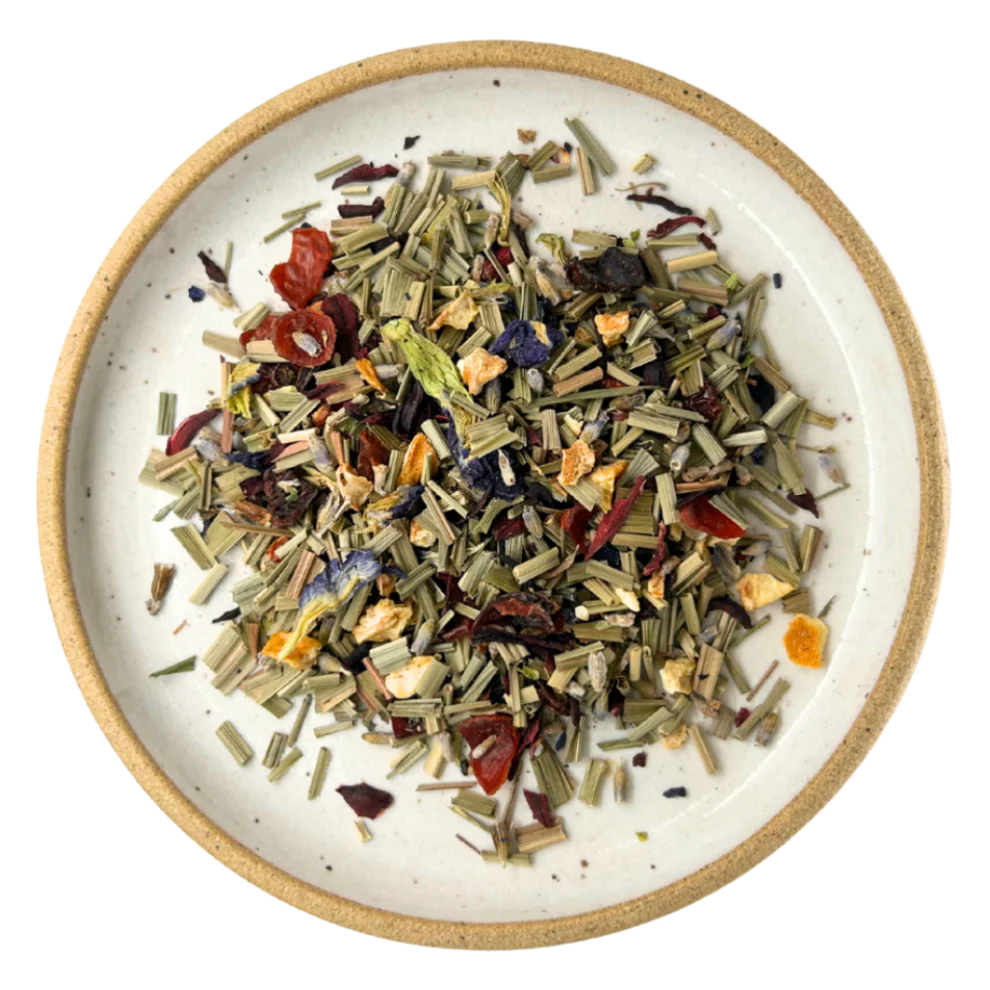 A top-down view of loose-leaf herbal tea mixed in a round speckled ceramic bowl with a natural beige rim, set against a solid white background. Available at Luca Essentials in Los Angeles. 