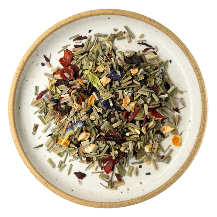 A top-down view of loose-leaf herbal tea mixed in a round speckled ceramic bowl with a natural beige rim, set against a solid white background. Available at Luca Essentials in Los Angeles. 