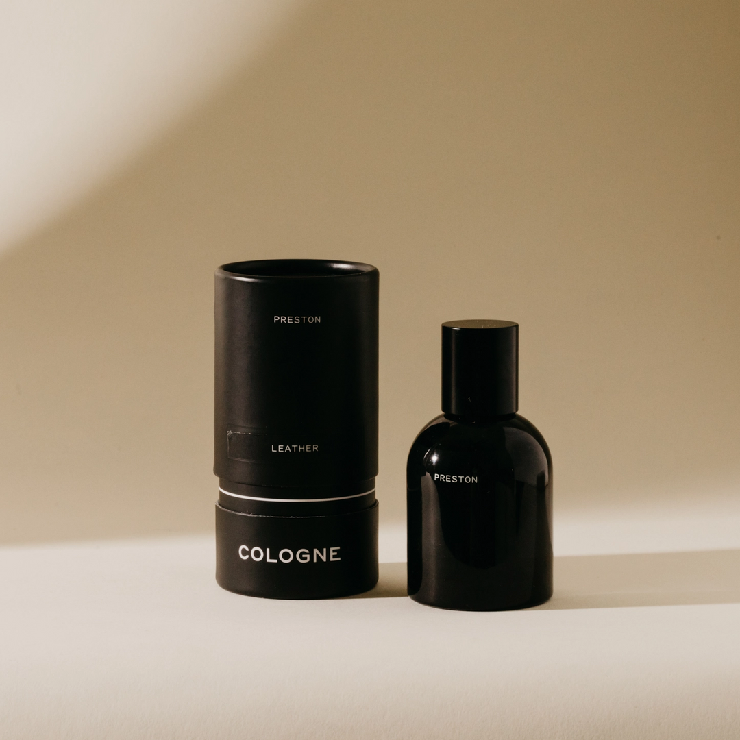 One black cologne bottle with a cylindrical package on a beige background. Available at Luca Essentials in Los Angeles. 
