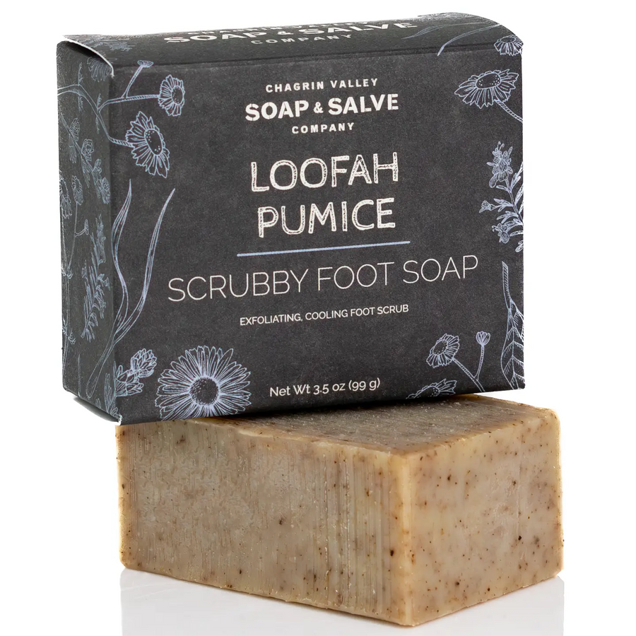 A bar of Chagrin Valley Soap & Salve Company Loofah Pumice Scrubby Foot Soap stacked in front of its dark charcoal gray box with white floral line art and text. Available at Luca Essentials in Los Angeles. 