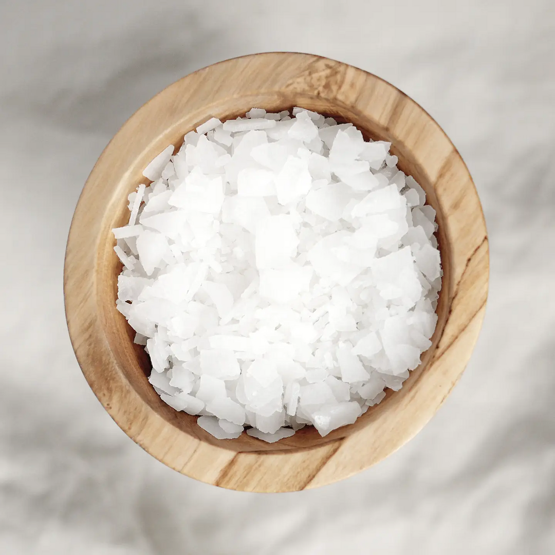 Wooden bowl filled with white magnesium flakes on a light gray background. Available at Luca Essentials in Los Angeles.