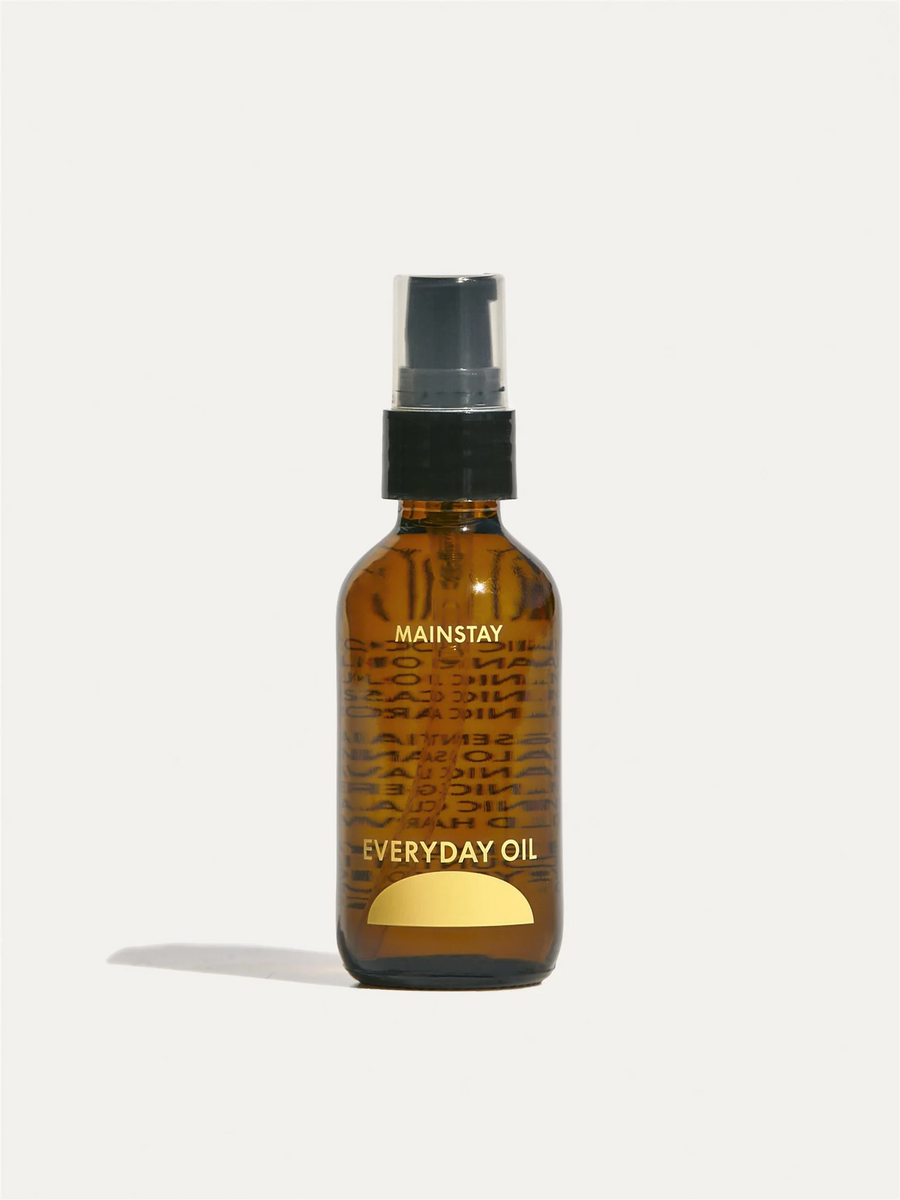 A 2oz amber bottle of oil with yellow logo and label, black pump top with a plastic lid on a white background. Available at Luca Essentials in Los Angeles. 
