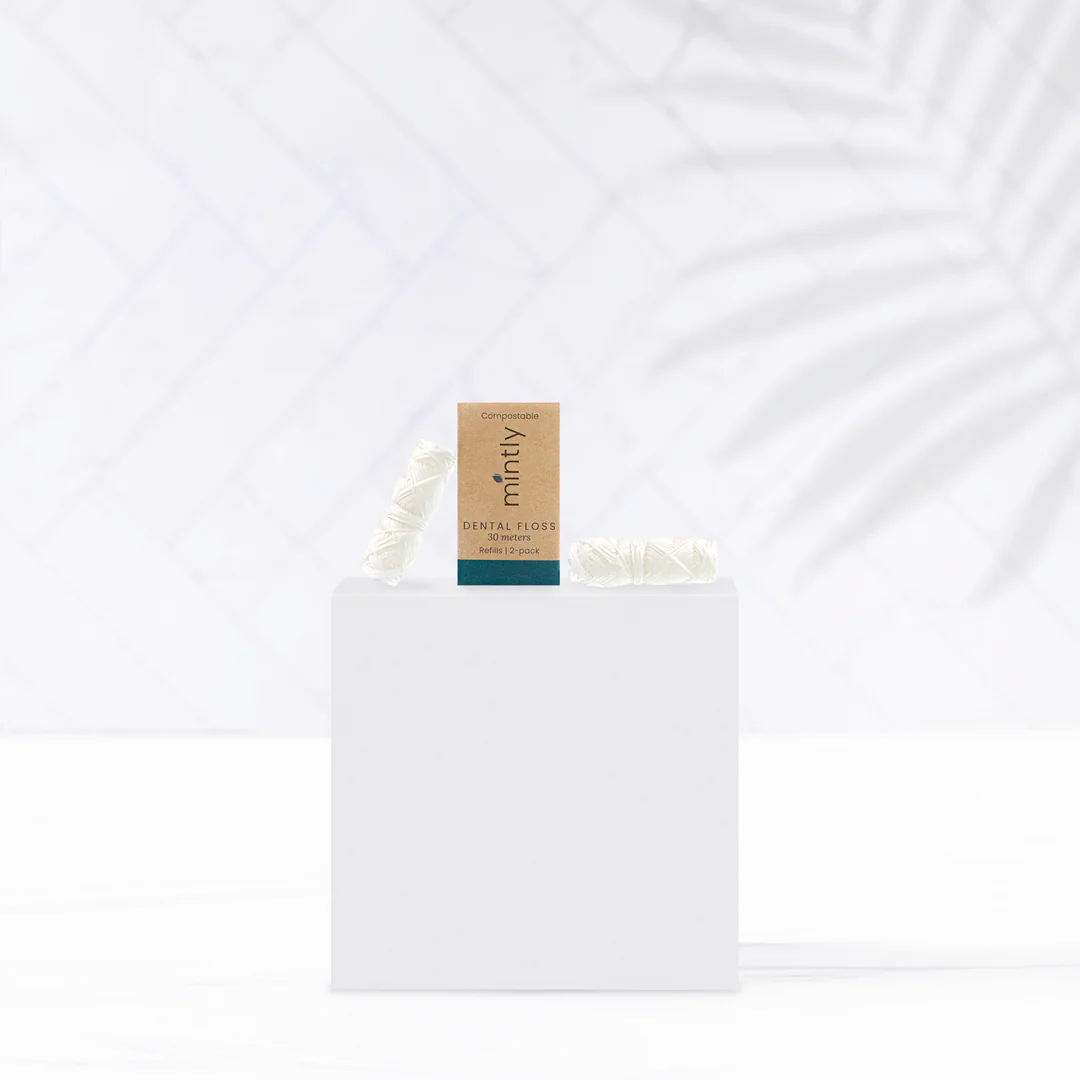 Two rolls of dental floss refills next to their packaging box, which reads 'Mintly' and has a 'compostable' label. Mintly is available at Luca Essentials in Los Angeles.