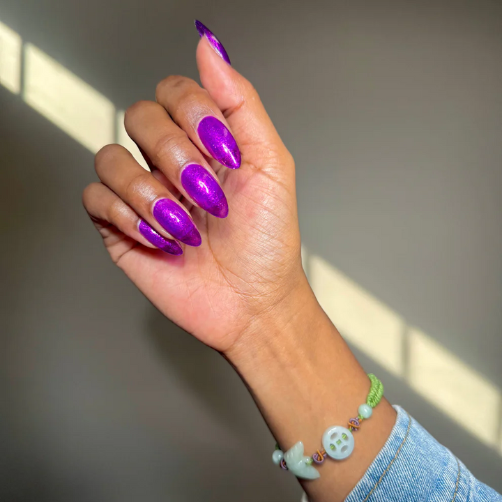 Hand with purple nail polish wearing a denim jacket and colorful bracelet. Available at Luca Essentials. 