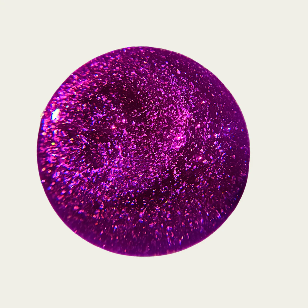 Purple glittery swatch of nail polish on a light gray background. Available at Luca Essentials in Los Angeles. 