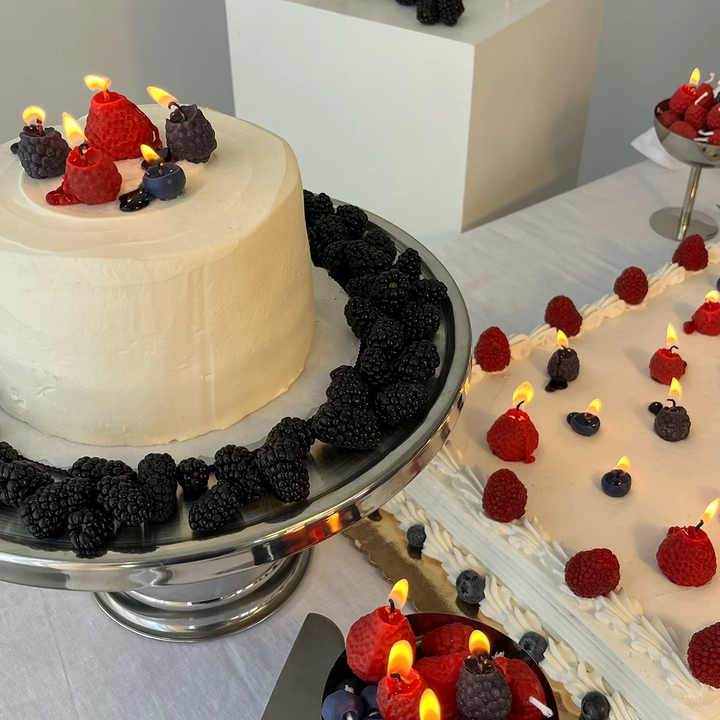 Two cakes with blueberry, raspberry, strawberry and blackberry shaped candles lit on both cakes, surrounded by real edible berries on the cakes. Available at Luca Essentials in Los Angeles. 