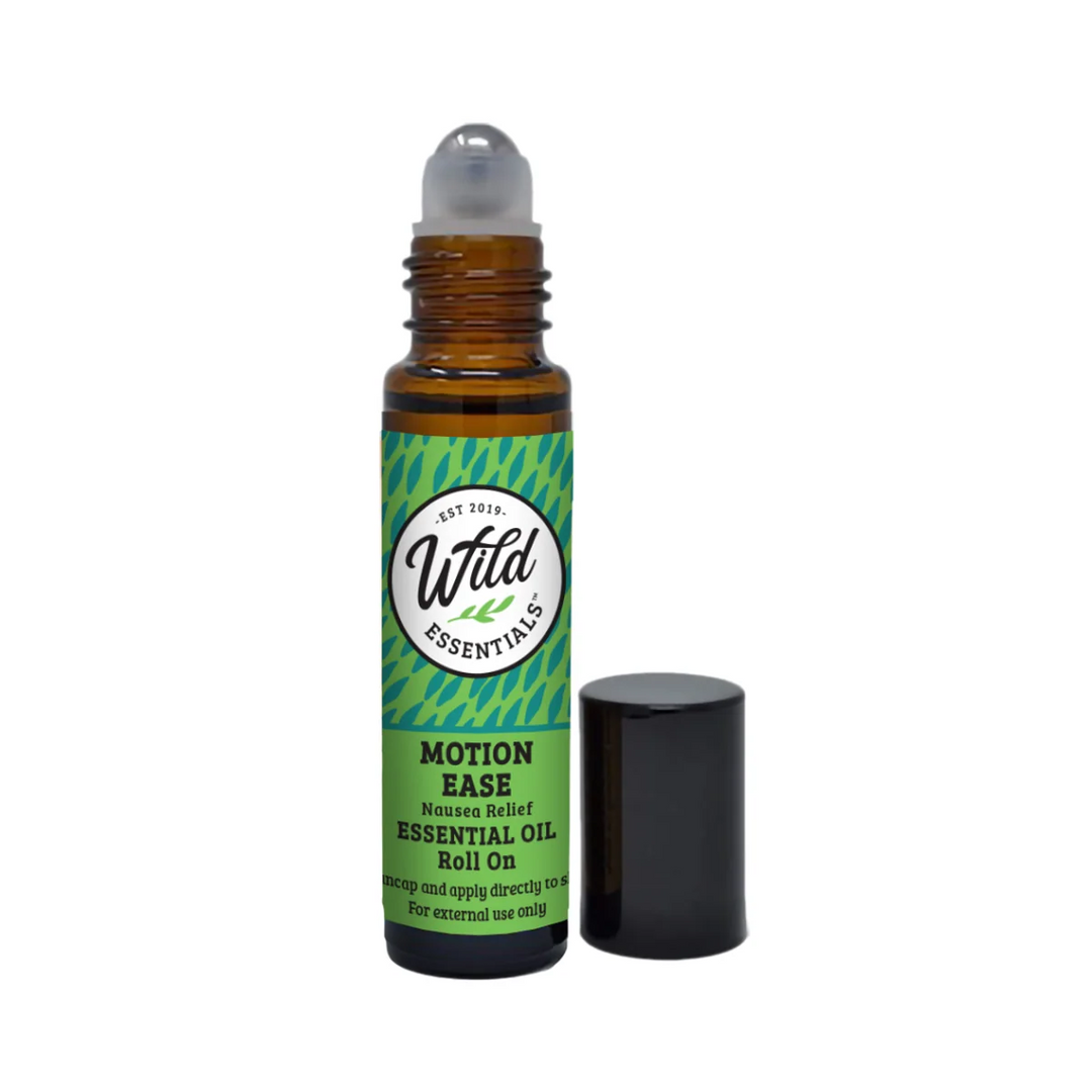 A roll-on essential oil bottle with its cap removed and placed beside it on a plain white background. The amber glass bottle has a green and teal label reading 'Wild Essentials' and 'Motion Ease Mesmerizing Relief Essential Oil Roll On. Available at Luca Essentials in Los Angeles.